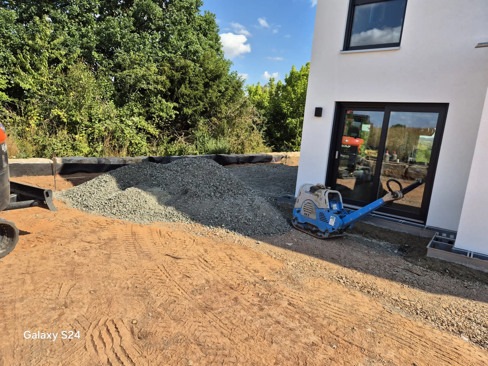 Schotter für den Flächenaufbau und eine Rüttelplatte neben dem Wohnhaus